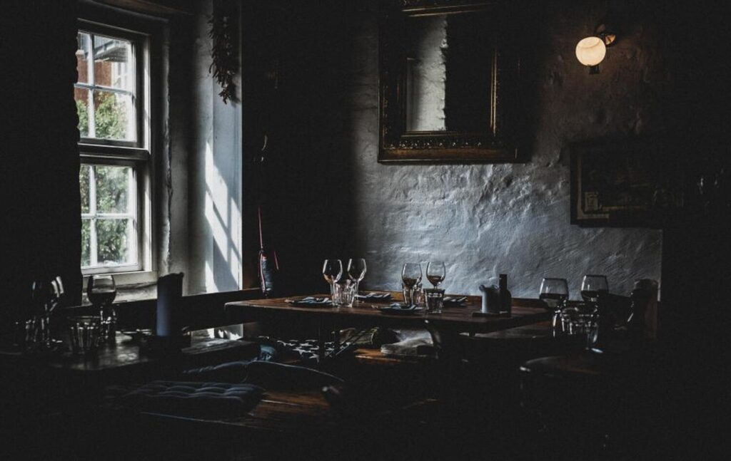 Comedor en penumbra de Vespra, con muros de piedra encalada y mesas vestidas de lino junto al ventanal